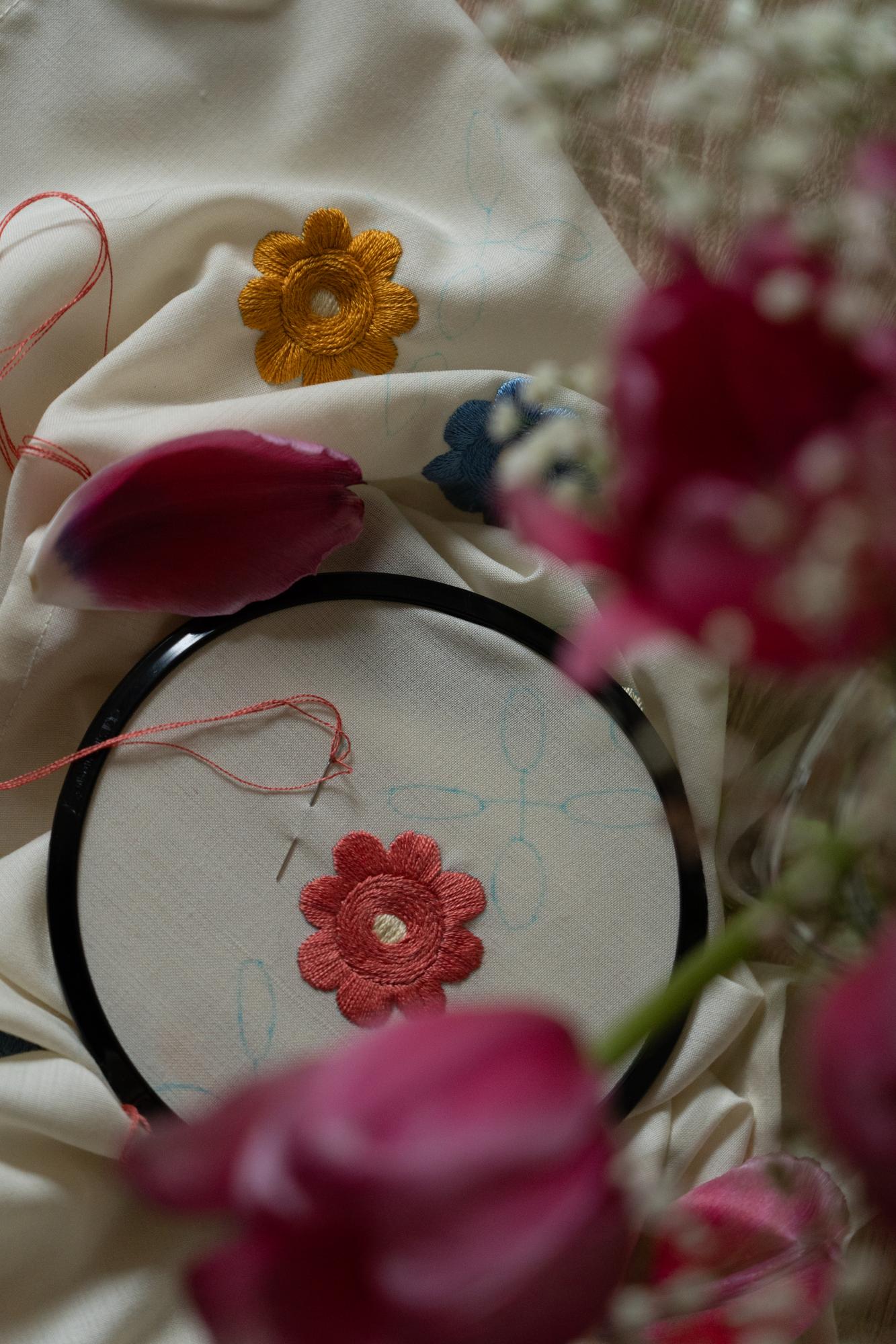 Mano che ricama un fiore con filo color crema